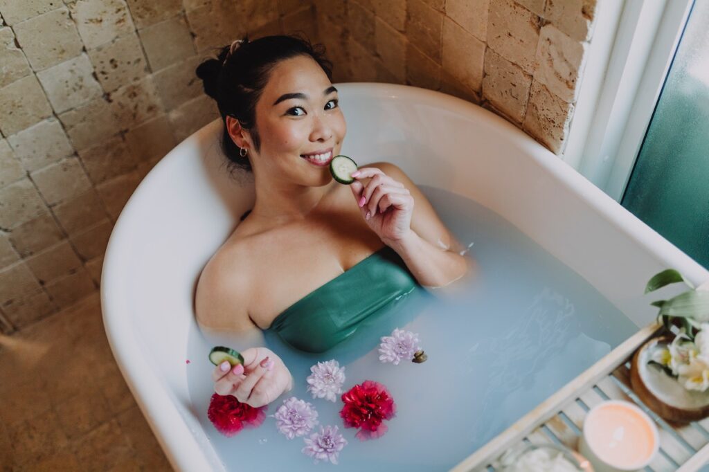 お風呂に花やキュウリを浮かべて優雅にお湯につかっている女性