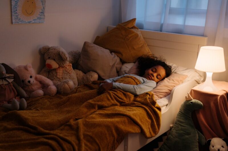 クッションや人形が並んだ自分の部屋のベッドで寝ている女の子