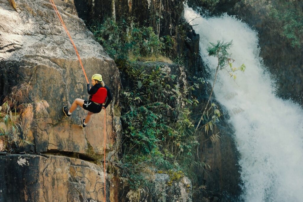 滝の横の断崖絶壁をロープで降りるヘルメットをかぶった女性