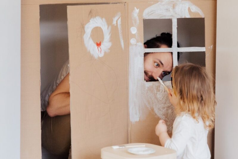 段ボールに家の絵を描いて遊んでいる女の子とお父さん